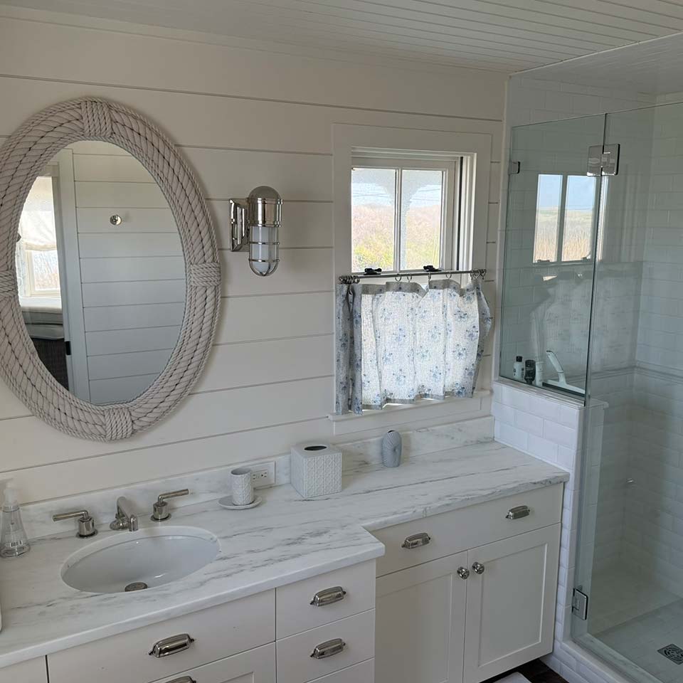 White bathroom with marble countertop, oval mirror, and updated window & door replacement accents.