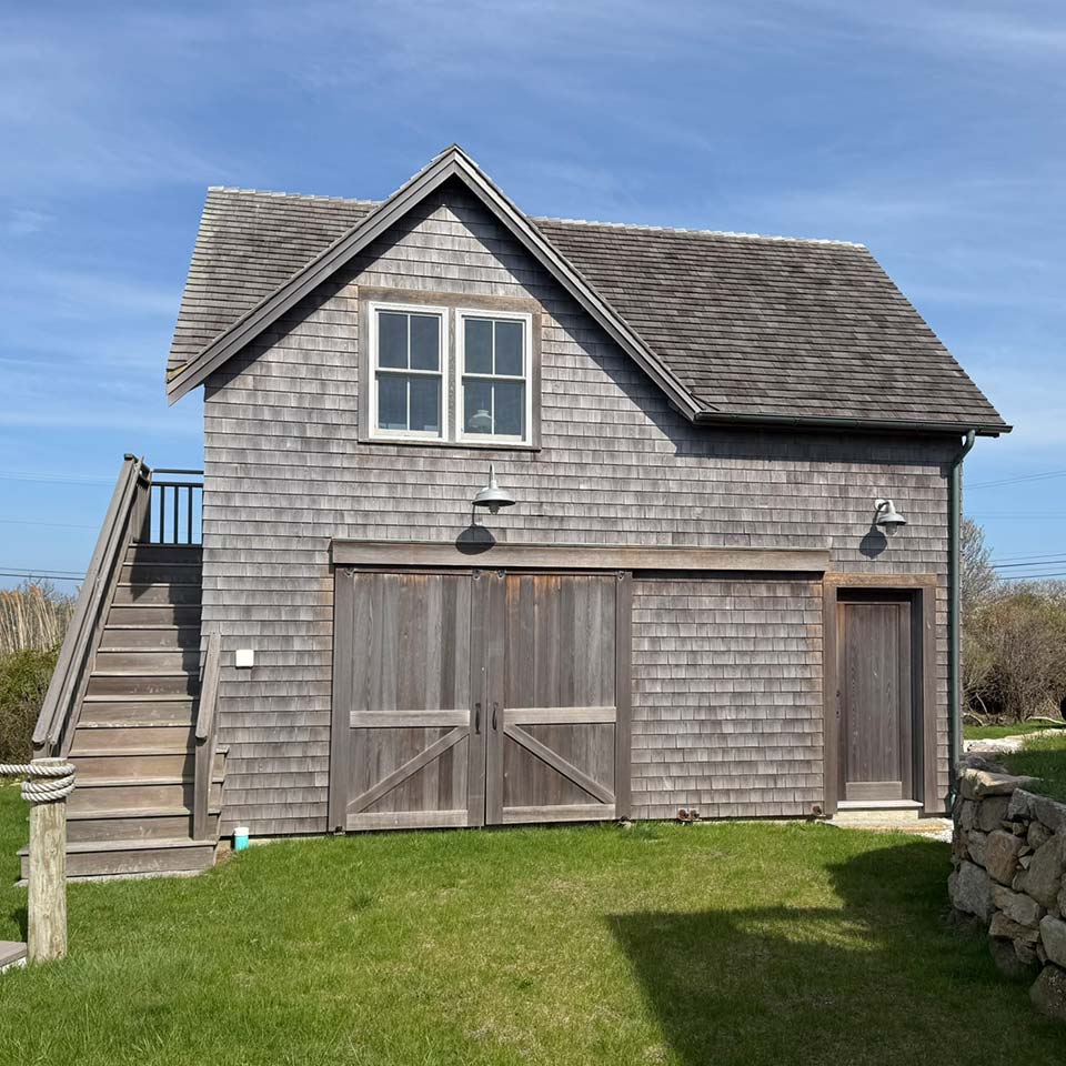 Two-story wooden shed with double doors, side stairs, and ideal for window & door replacement projects.